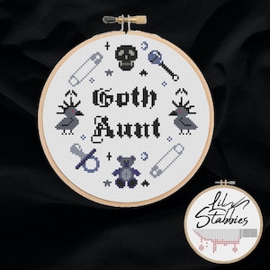 May include: White embroidery hoop with a cross stitch design of a skull, ravens, a teddy bear, a pacifier, safety pins, and the text "Goth Aunt".