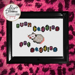 May include: Cross stitch pattern featuring a possum with the text "even baddies get saddies" in rainbow colors.
