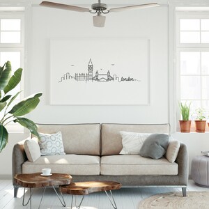 May include: A black and white line drawing of the London skyline, including Big Ben, the London Eye, and Tower Bridge. The drawing is framed and hanging on a white wall above a beige sofa with pillows. The word "london" is written in cursive below the skyline.