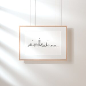 May include: A black and white line drawing of the London skyline, including Big Ben and Tower Bridge. The drawing is framed in a light wood frame and hanging on a white wall.
