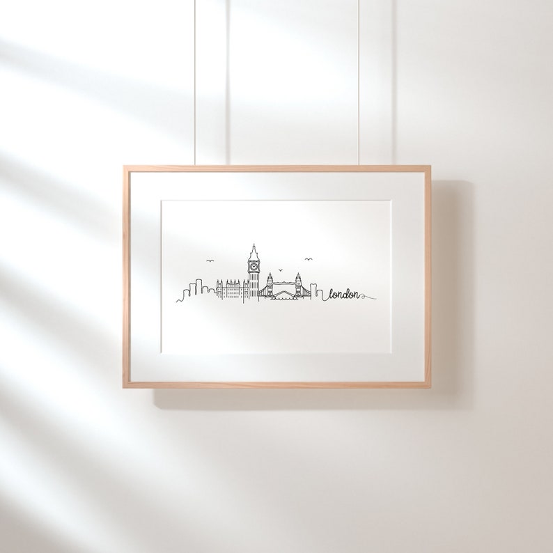May include: A black and white line drawing of the London skyline, including Big Ben and Tower Bridge. The drawing is framed in a light wood frame and hanging on a white wall.