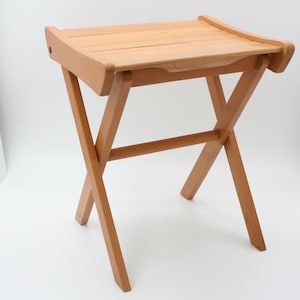 May include: A light brown wooden folding side table. The table has a rectangular top with a slatted design and rounded edges. The legs are in an X-shape, providing stability. The table is approximately 20 inches long, 15 inches wide, and 20 inches high.