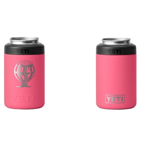 May include: Two pink YETI can insulators. One has a silver graphic of a beer glass with the word "ABED" inside. The other has the YETI logo in silver. Both have a black top and silver rim.