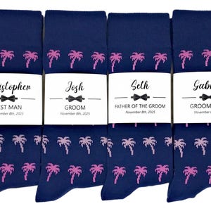 May include: Four pairs of navy blue socks with a pink palm tree pattern. Each sock has a white label with a name, title, and date. The names are Christopher, Josh, Seth, and Gabriel.