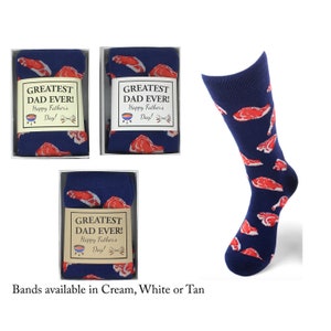 May include: Three boxes of blue socks with a red steak print. The socks have a white label with the text "Greatest Dad Ever! Happy Father's Day!" The boxes are on a white background. Bands available in Cream, White or Tan.