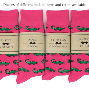 May include: Four pairs of pink socks with a green alligator pattern. Each sock has a brown label with a bow tie and the text "AUSTIN BEST MAN", "DANIEL GROOM", "CHRISTIAN GROOMSMAN", and "BRANDON USHER".