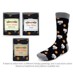 May include: Three gift boxes with different holiday greetings: "Season's Greetings", "Merry Christmas", and "Happy Holidays". Each box contains a pair of black socks with a basketball and hoop pattern. The socks have a gray cuff.