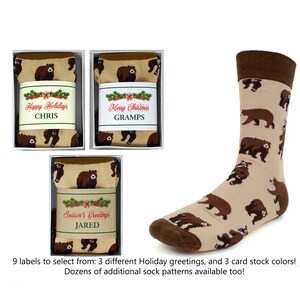 May include: Three gift boxes with socks featuring a brown bear pattern. The boxes have labels with different holiday greetings: "Happy Holidays", "Merry Christmas", and "Season's Greetings".