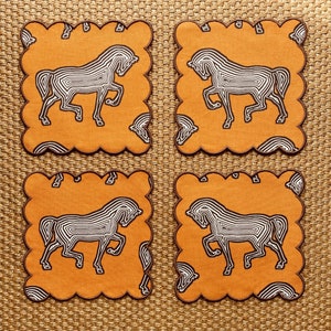 May include: Four orange and brown fabric coasters with a white stylized horse design. The coasters have a scalloped edge.