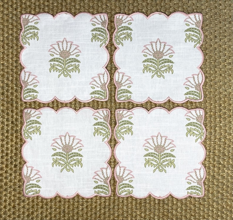 May include: Set of four pink and green floral embroidered linen napkins. The napkins have a scalloped edge and feature a delicate floral design.