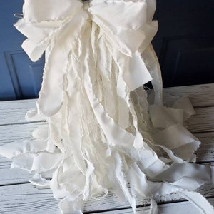 May include: A large white bow with frayed edges and long, flowing tails. The bow is made of fabric and is perfect for adding a touch of elegance to any occasion.
