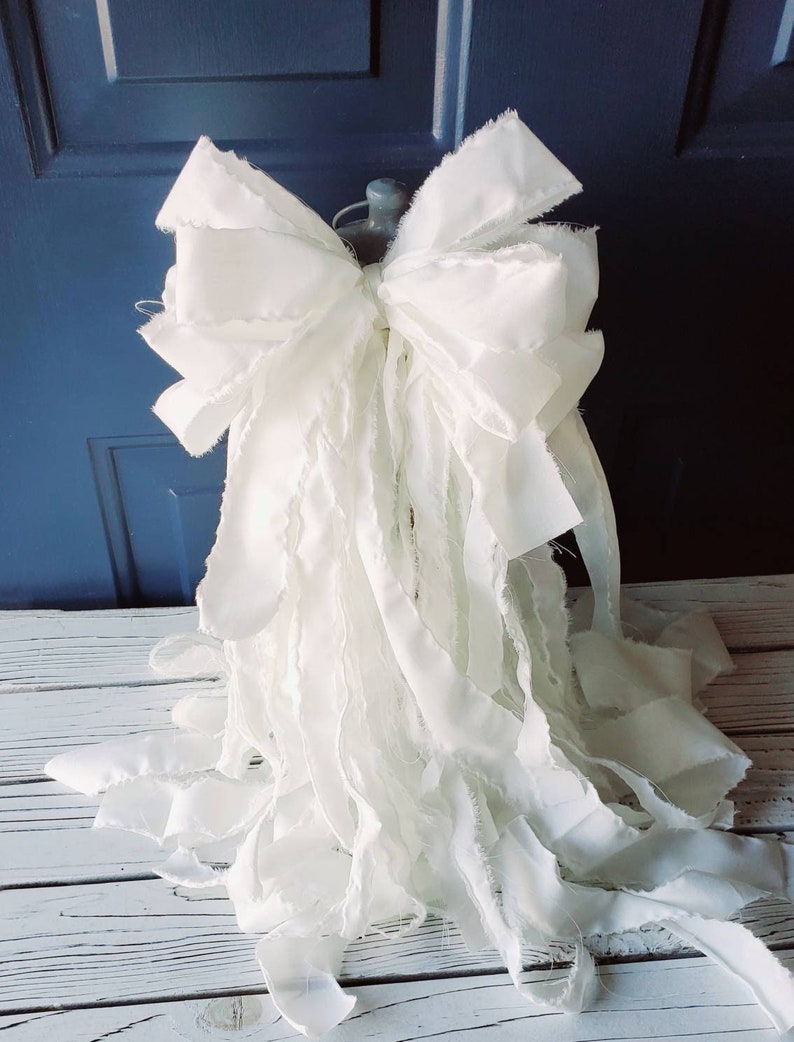 May include: A large white frayed ribbon bow, perfect for a Christmas tree topper or a decorative accent.