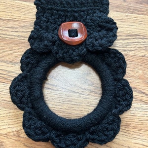 May include: Black crocheted pot holder with a wooden button. The pot holder has a scalloped edge.
