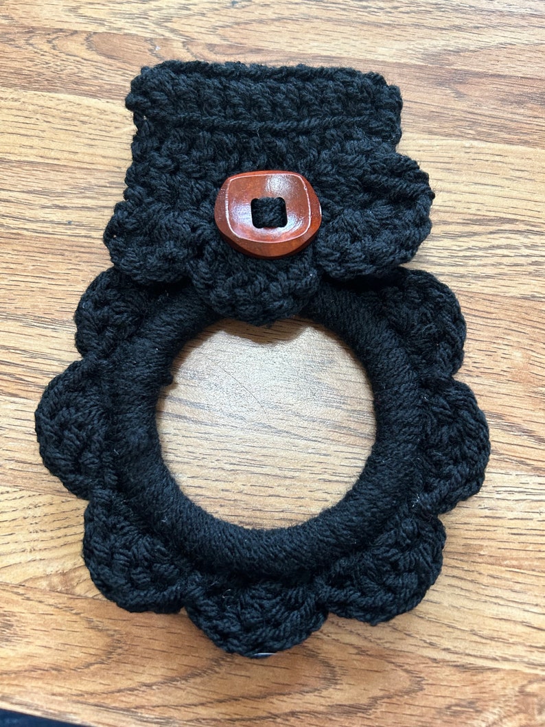 May include: Black crocheted pot holder with a wooden button. The pot holder has a scalloped edge.