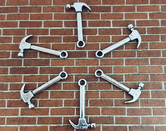 May include: Six silver-toned miniature hammers arranged in a star shape against a brick wall background.