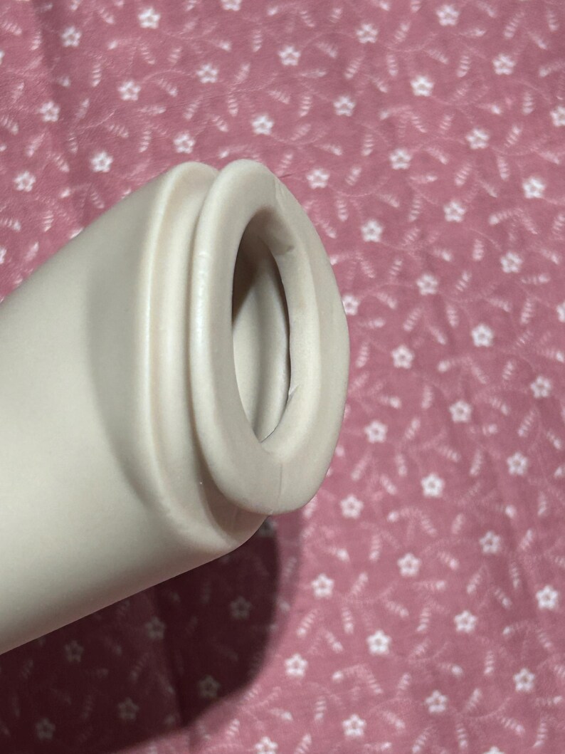 May include: A cylindrical, off-white, smooth-textured object with a rounded, protruding rim at the opening. The object features a hollow center and a uniform, matte finish, showing a simple, functional design with no additional markings or patterns.