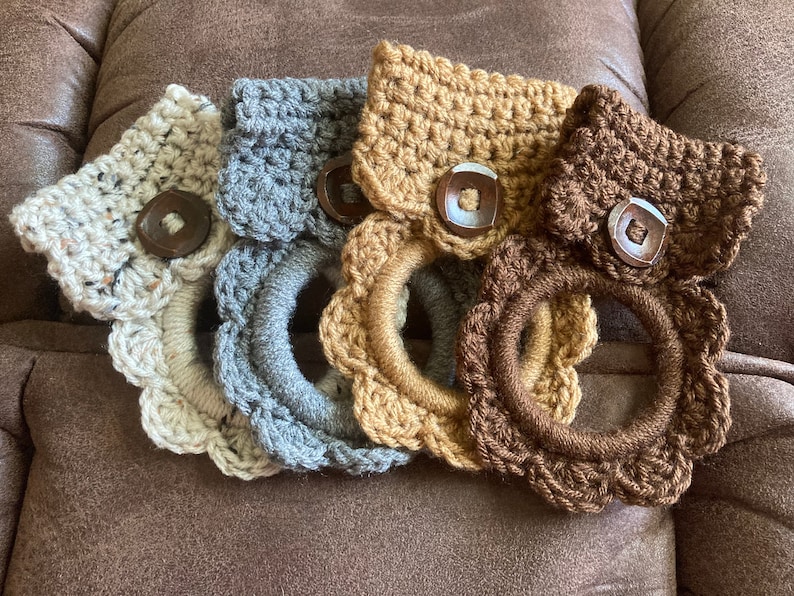 May include: Four crocheted towel rings with wooden buttons. The rings are in beige, gray, brown, and tan.