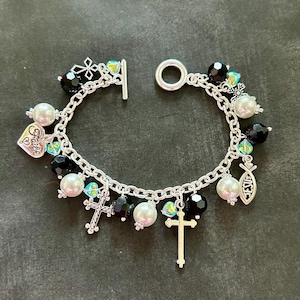 May include: A silver charm bracelet with black and white beads, silver crosses, and charms that say "Faith" and "Jesus".