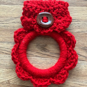 May include: Red crocheted dishcloth with a wooden button. The dishcloth is in the shape of a circle with a scalloped edge.