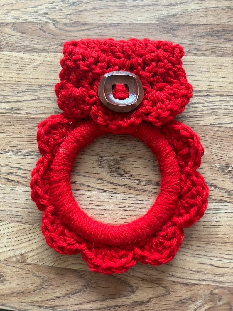 May include: Red crocheted dishcloth with a wooden button. The dishcloth is in the shape of a circle with a scalloped edge.