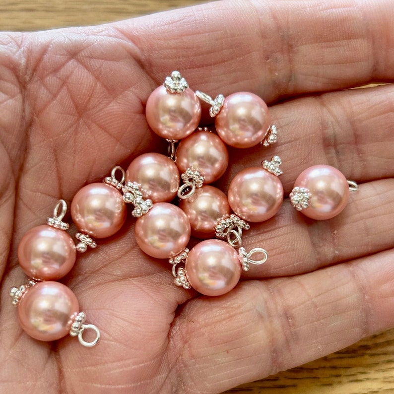 May include: A collection of pale pink pearl beads with silver accents. Each bead has a small loop for attaching to a jewellery project.