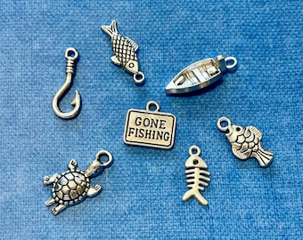 May include: A set of silver charm pendants with fishing themes. The charms include a fish, a boat, a hook, a turtle, a fish skeleton, and a sign that says "Gone Fishing".