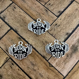 Puede incluir: Tres abalorios de plata con esmalte negro y las palabras "Born to Ride" en una fuente estilizada.