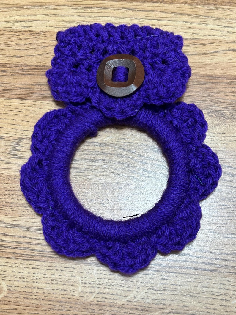 May include: Purple crocheted pot holder with a wooden button. The pot holder is shaped like a flower with a scalloped edge.