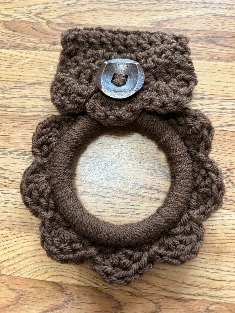 May include: Brown crocheted pot holder with a brown button. The pot holder is shaped like a ring with a scalloped edge.