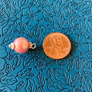 May include: A pink oval pearl bead with a silver clasp, next to a US penny for size comparison. The penny is dated 2018.