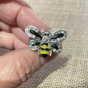 May include: A silver ring with a black and yellow bee design. The bee has clear rhinestones on its wings.