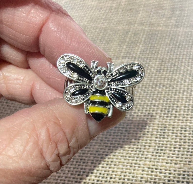 May include: A silver ring with a black and yellow bee design. The bee has clear rhinestones on its wings.