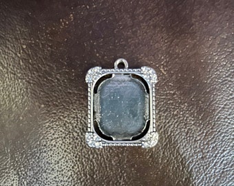 May include: Silver pendant with a clear glass or plastic insert. The pendant has a decorative border of small rhinestones.