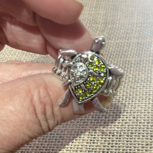 May include: A silver ring with a green and clear crystal turtle charm. The ring is adjustable and has a braided band.