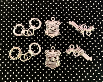 May include: Six silver-toned charms, including two pairs of handcuffs, two police badges with the words "Police Dept." and an eagle, and two silver-toned pistols.