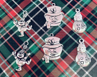 May include: Six silver charm pendants featuring snowman designs. The charms are on a red and green plaid background.