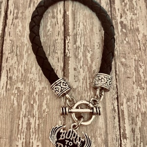 Puede incluir: Pulsera trenzada de cuero negro con cierre de palanca plateado y un dije plateado que dice "Born to Ride" con alas.
