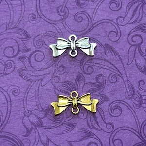 May include: Two metal bow charms, one silver and one gold. Both charms have a loop on each side for attaching to jewelry or other crafts.