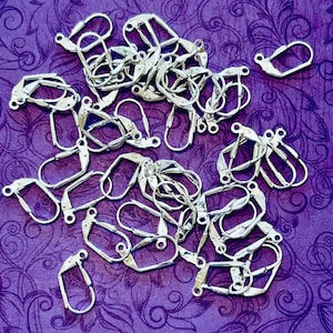 May include: A large pile of silver earring hooks, also known as ear wires, on a purple background. The hooks are made of metal and have a spring-loaded closure.