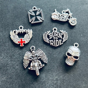 May include: Six silver charms with different designs. The charms include a motorcycle, a skull, a cross with wings, a cross, a motorcycle with wings, and a charm with the words "Born to Ride".