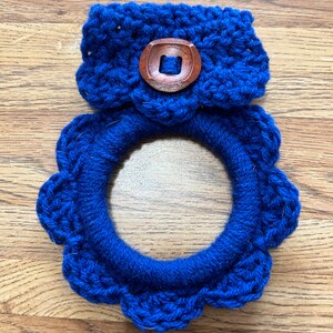 May include: A blue crocheted wreath with a blue crocheted band and a wooden button in the center.
