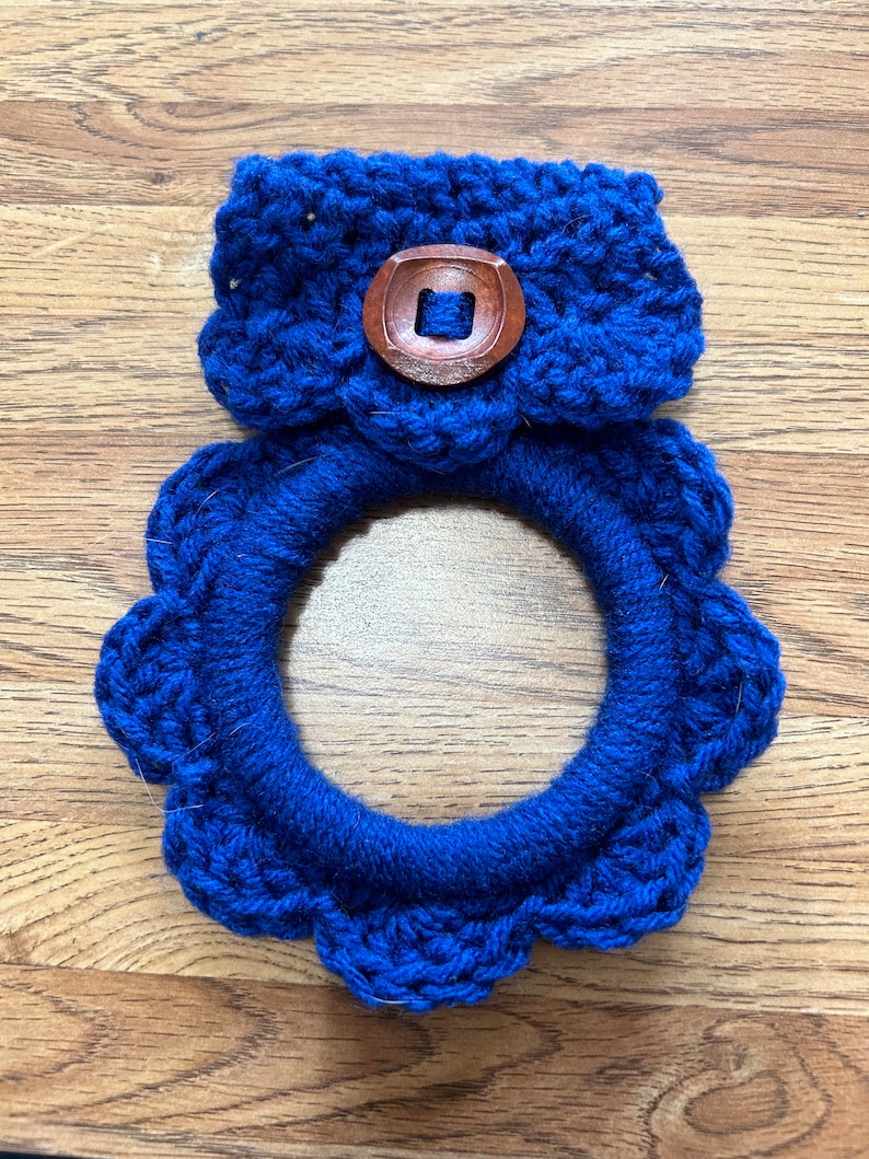 May include: A blue crocheted wreath with a blue crocheted band and a wooden button in the center.