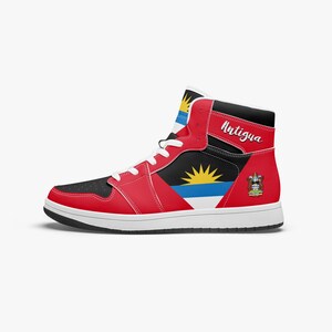 Può includere: Sneaker alta con il design della bandiera di Antigua e Barbuda. La scarpa ha una combinazione di colori rosso, nero e bianco con la scritta "Antigua" sul lato. La suola e i lacci sono bianchi.