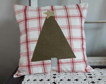 May include: Square pillow with a red and white plaid pattern. A large olive green felt Christmas tree is centered on the pillow, topped with a tan star. The tree has a gray trunk. The pillow is on a white lace surface.