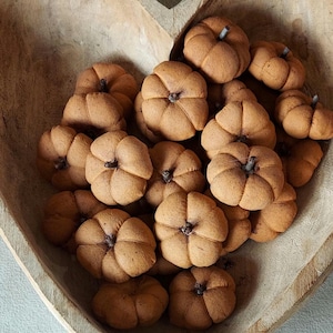 May include: A heart-shaped wooden bowl filled with small, brown, pumpkin-shaped decorations. Each pumpkin has a stem and is clustered together, creating a fall-themed display. The bowl's natural wood grain adds to the rustic aesthetic.