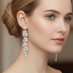 Puede incluir: Pendientes colgantes plateados con diseño de hojas. Cada pendiente presenta múltiples cristales claros y brillantes dispuestos en un patrón en cascada. Los pendientes están diseñados para colgar y captar la luz, añadiendo glamour.