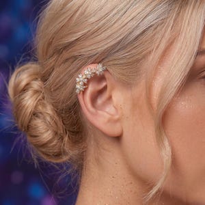 Può includere: Un ear cuff floreale con accenti scintillanti. L'ear cuff è composto da piccoli fiori delicati e cristalli, creando un look glamour ed elegante. Il gioiello si curva lungo l'orecchio, aggiungendo un tocco di brillantezza e raffinatezza.