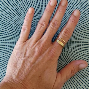 Pode incluir: Close-up de uma mão com duas finas bandas douradas no dedo anelar.