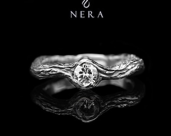May include: A silver ring with a diamond set in a branch-like band. The ring is on a black background and reflects light.