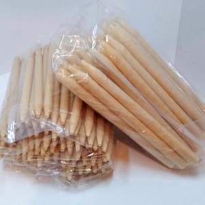 Puede incluir: Dos bolsas de plástico transparente llenas de velas para oídos beige. Las velas son largas, cilíndricas y afiladas en un extremo. Las bolsas están sobre una superficie blanca. Las velas parecen estar hechas de un material enrollado.
